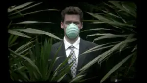 A man in a mask looking at the camera surrounded by palm trees